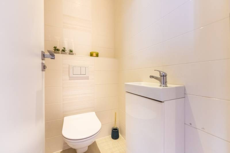 Badezimmer mit Waschbecken und Toilette in einem Einfamilienhaus, helle Fliesen, Dekorationen.