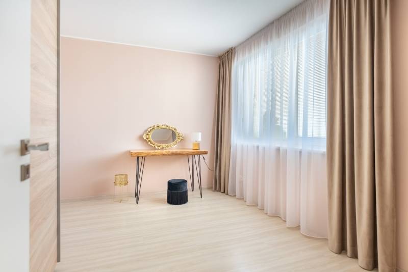 Helles Zimmer in einem Einfamilienhaus mit Schminktisch, goldenem Spiegel und Boden in Holzoptik.