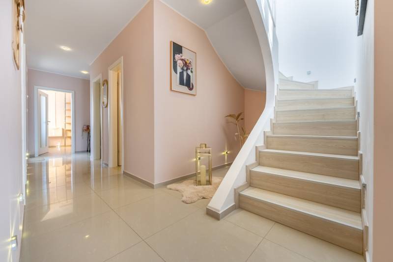 Ein Flur in einem Einfamilienhaus mit Fliesen, einer Treppe und Dekorationen an den Wänden.