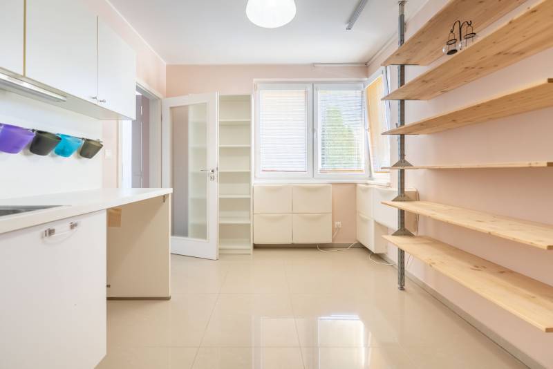 Innenraum eines Einfamilienhauses mit Regalen, Küchenzeile und großen Fenstern mit Rollläden.