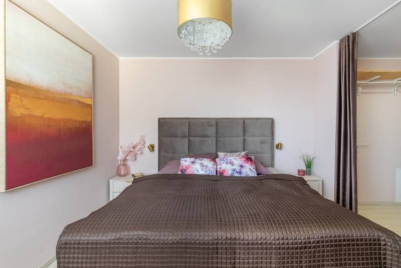 Schlafzimmer mit breitem Bett, dekorativen Kissen, Bild und verstecktem Stauraum in einer Vierzimmerwohnung.