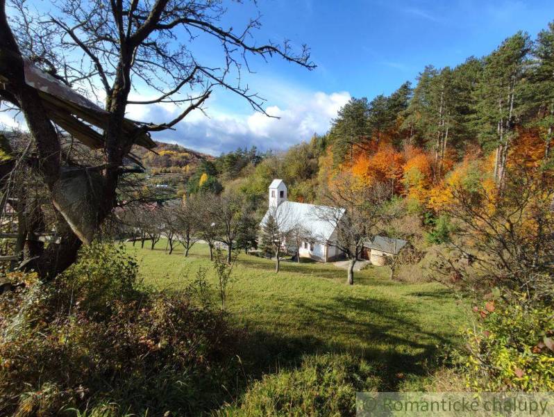 Herbst in den Gärten von Hlboké nad Váhom mit einer kleinen Kirche zwischen den Bäumen, bunte Wälder im Hintergrund.