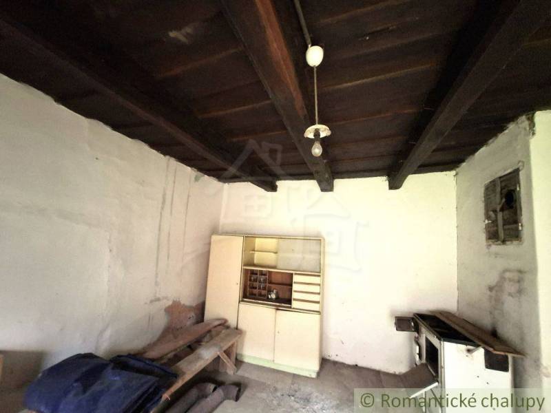 Innenraum eines Einfamilienhauses mit Holzbalkendecke, weißem Schrank und altem Herd.