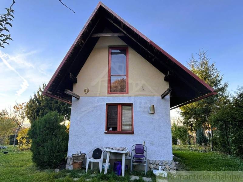 Hütte in Sološnica mit steilem Dach, Fenster, Natur und Plastikstühle.