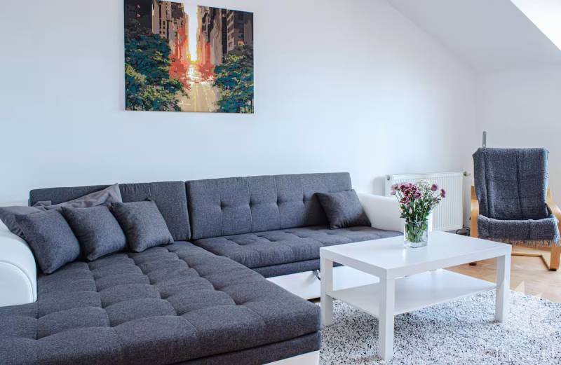 Wohnzimmer mit grauem Sofa, weißem Tisch und Blumen in einer 3-Zimmer-Wohnung.