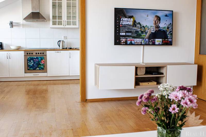 Küche in einer 3-Zimmer-Wohnung mit einem Fernseher an der Wand und Blumen auf dem Tisch.