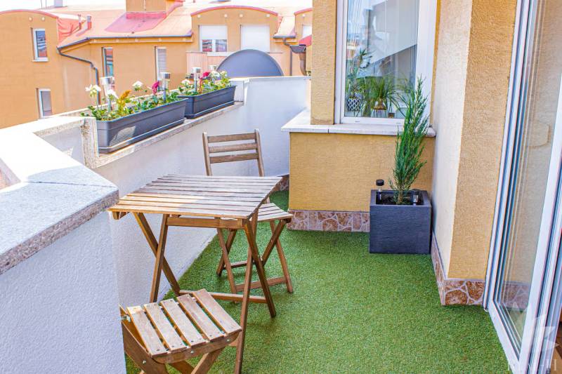 Balkon in einer 3-Zimmer-Wohnung mit Sitzgelegenheiten und Pflanzen auf Kunstrasen.