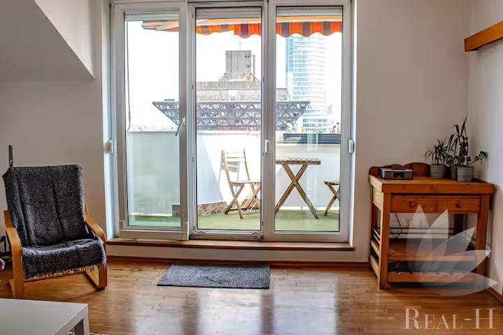 Wohnzimmer mit Balkon, Holzboden, Stuhl und Tisch in einer 3-Zimmer-Wohnung.