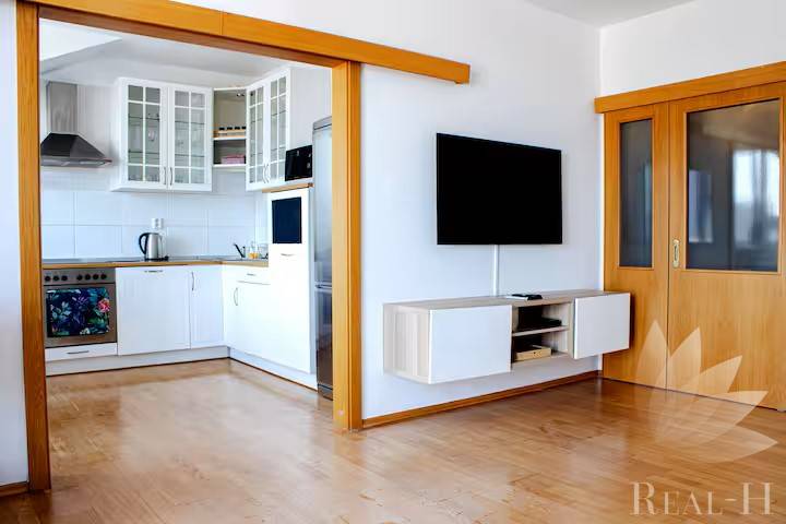 Wohnzimmer in einer 3-Zimmer-Wohnung mit Durchgang zur Küche und Wandfernseher.