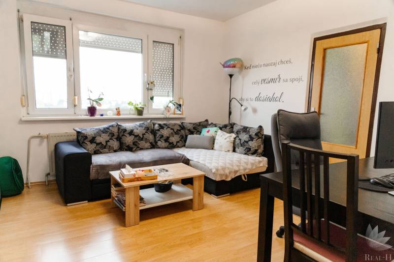 Wohnzimmer in einer 2-Zimmer-Wohnung mit einer Eckcouch und einem Boden in Holzoptik.