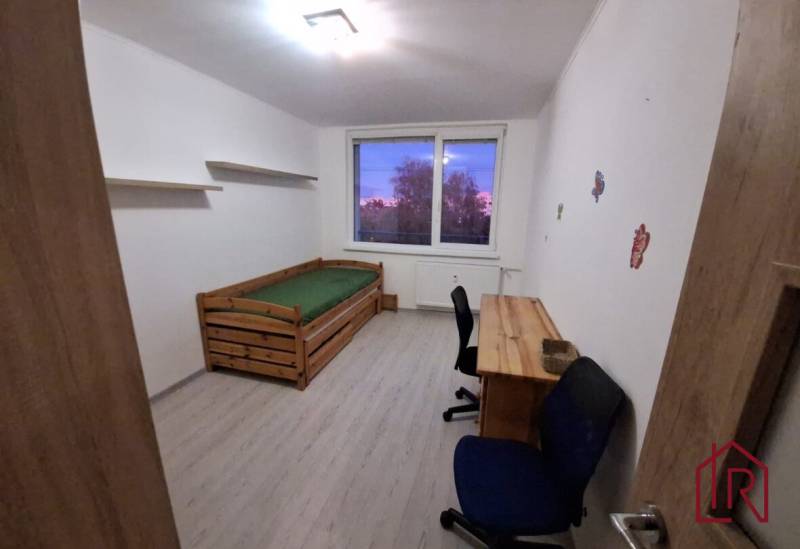 Ein Zimmer mit Bett und Tisch in einer 3-Zimmer-Wohnung, mit einem Boden in Holzoptik.