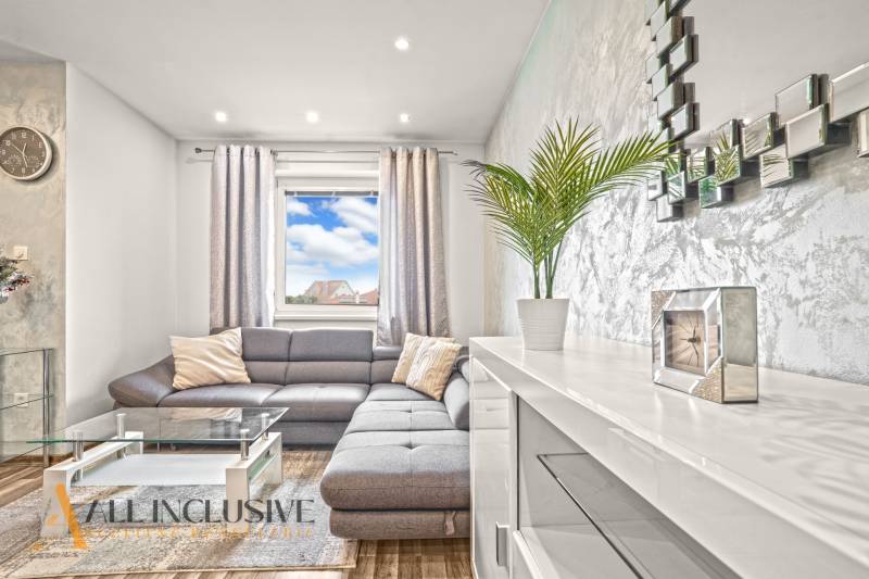 Wohnzimmer mit grauem Sofa, Glastisch und Holzboden.