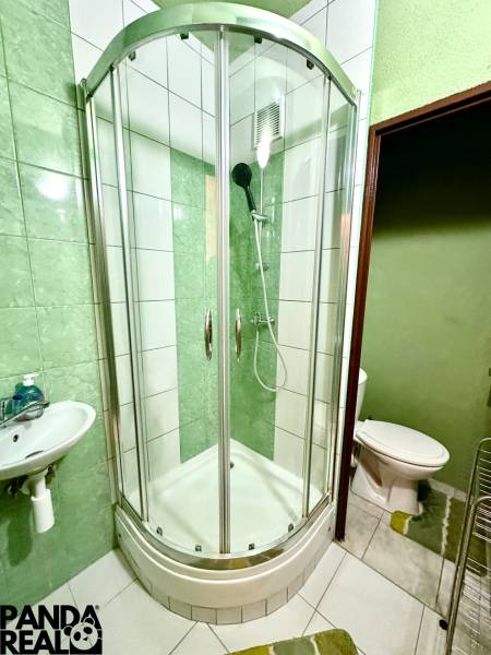 Badezimmer in einem Studio-Apartment mit einer Eckdusche, einem Waschbecken und weißen Fliesen.