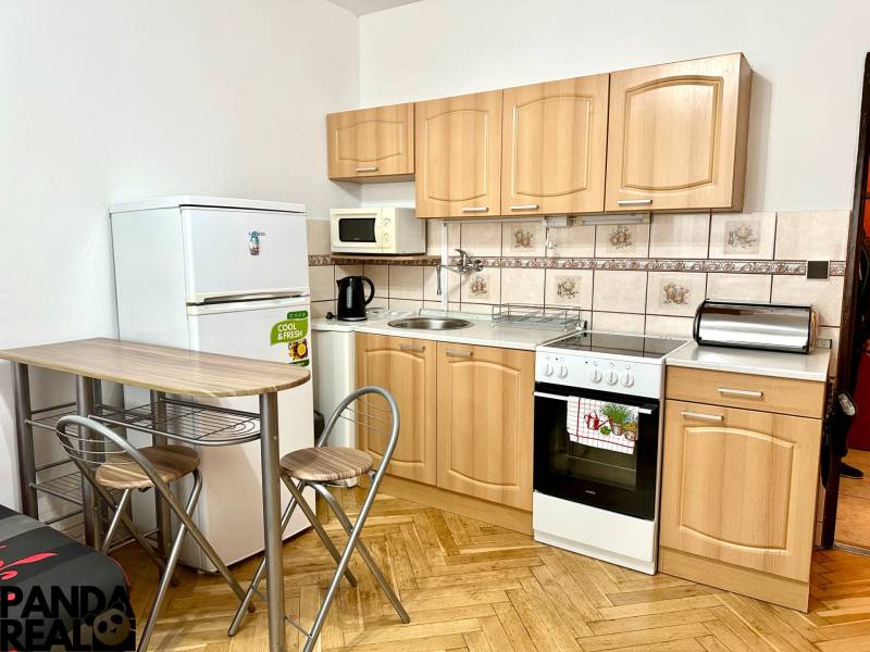 Küche in einem Einzimmerapartment mit Holzboden, Geräten und Sitzgelegenheiten.