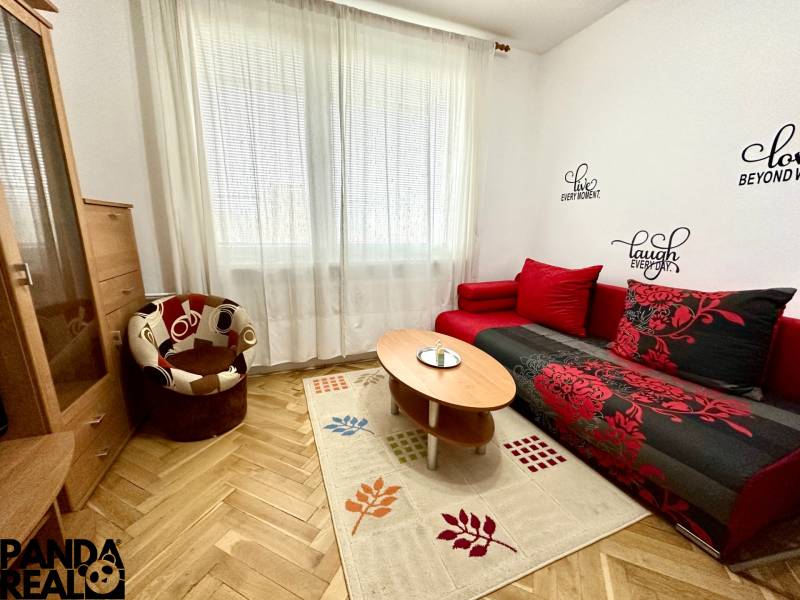 Ein Studio mit einem Boden in Holzoptik, einem roten Sofa und einem Sessel.