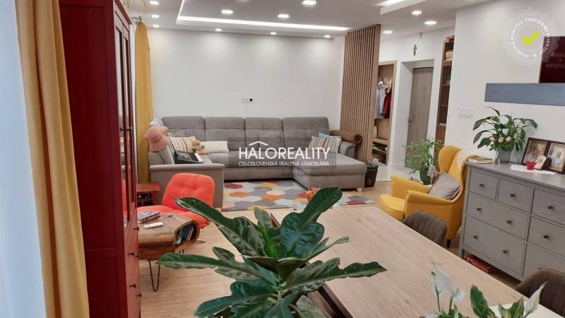 Wohnzimmer in einer 3-Zimmer-Wohnung mit Sitzbereich, Blumen und einem Boden in Holzoptik.