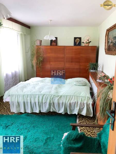 Schlafzimmer in einem Einfamilienhaus mit Holzmöbeln, grünem Teppich und Pflanzen.