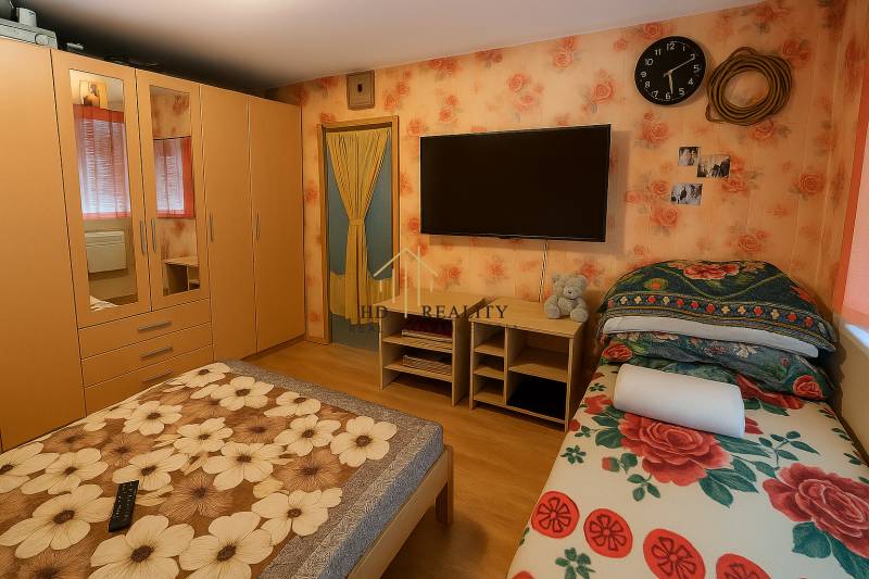 Schlafzimmer mit Blumen-Tapete, Schrank, Bett und Holzboden in einer 2-Zimmer-Wohnung.