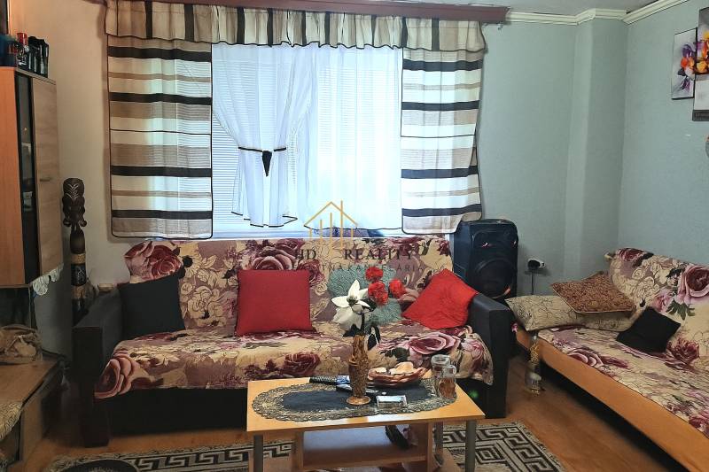 Wohnzimmer in einer Zweizimmerwohnung mit gemusterten Sofas und Holzboden.