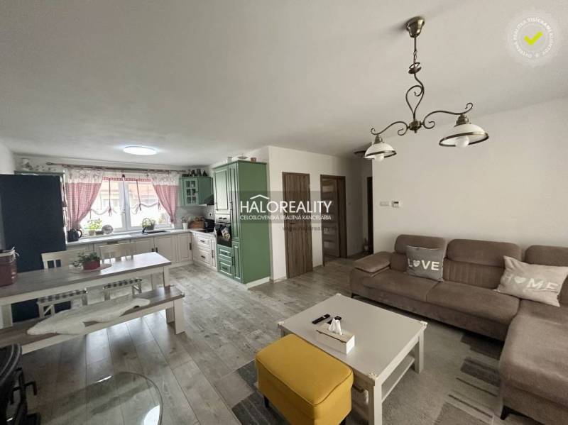 Obývačka v rodinnom dome so sedacou súpravou, stolom a kuchynskou linkou.