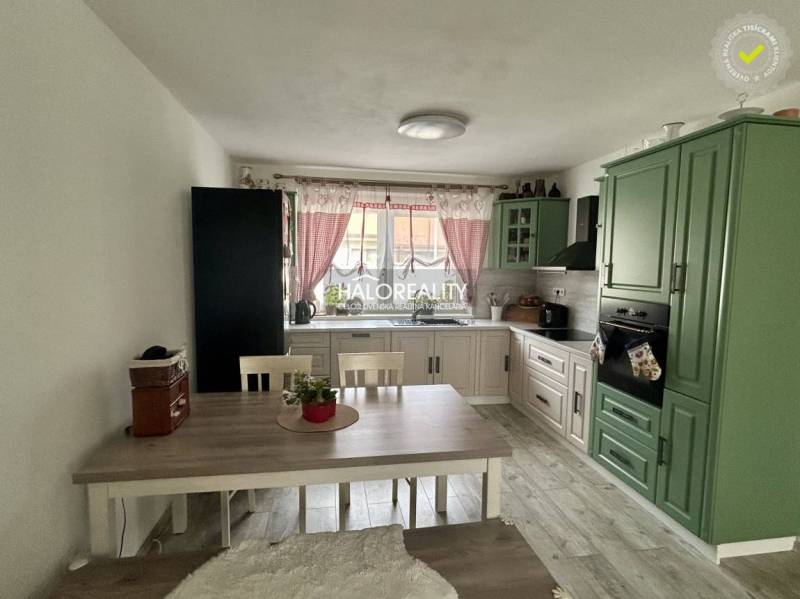 Küche in einem Einfamilienhaus mit grüner Küchenzeile, Esstisch und roten Vorhängen.