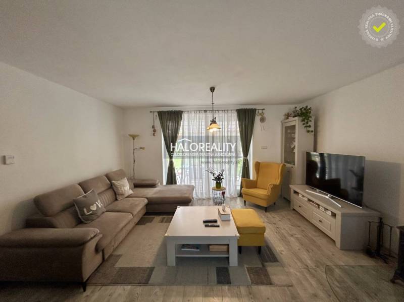 Wohnzimmer in einem Einfamilienhaus mit Sofa, Sessel, Fernseher und Blumen.