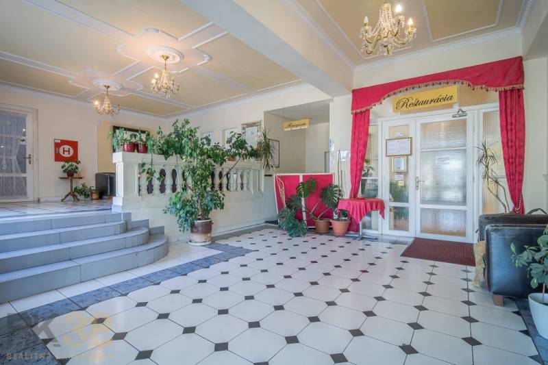 Hotelrezeption mit Pflanzen und Kronleuchtern, Fliesen mit geometrischem Muster.