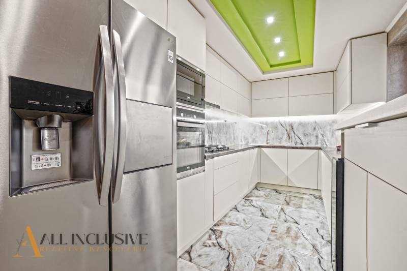 Eine Küche in einem Einfamilienhaus mit weißen Schränken, einer Marmor-Rückwand und einem Kühlschrank aus Edelstahl.