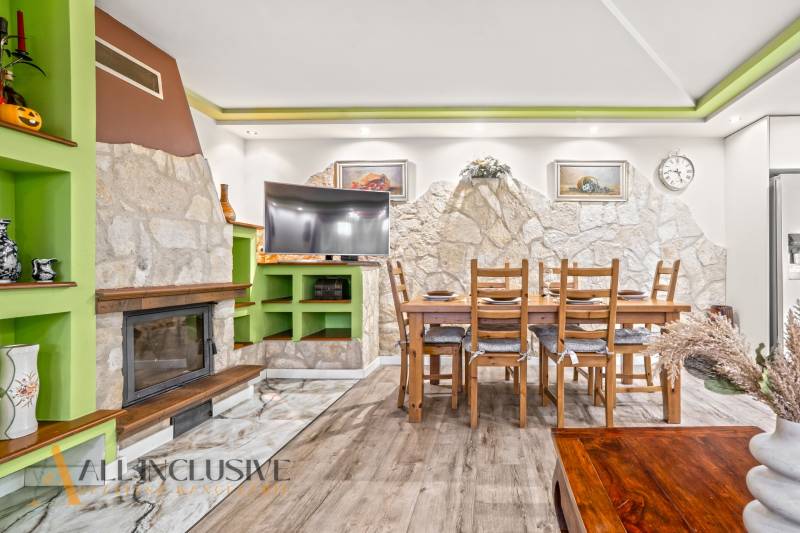 Innenraum eines Einfamilienhauses mit Kamin, Steinwand, Esstisch und Boden in Holzoptik.