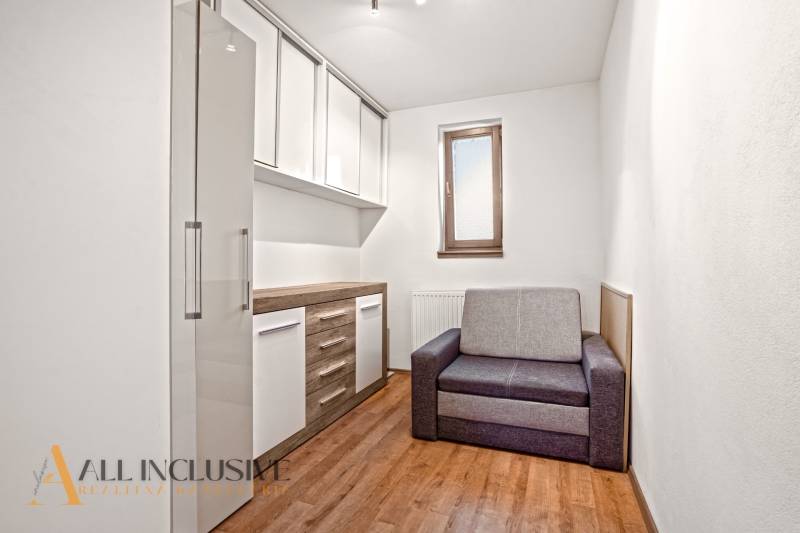 Ein Zimmer in einem Einfamilienhaus mit einem Boden in Holzoptik, einem grauen Sofa und Aufbewahrungsschränken.