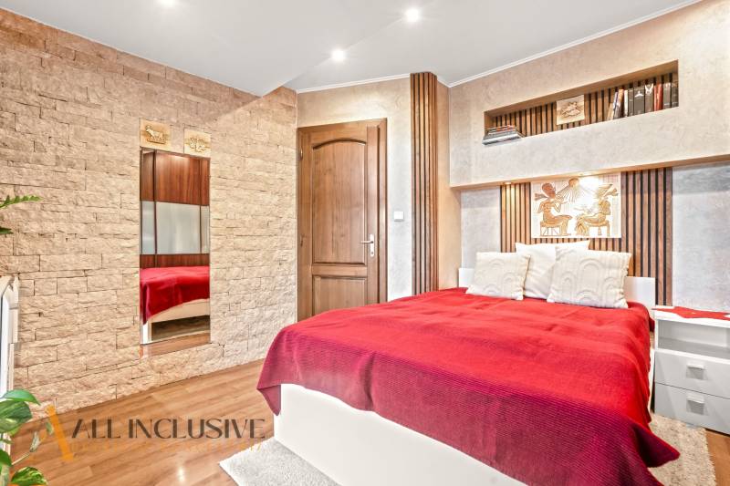 Schlafzimmer im Einfamilienhaus mit Bett, Steindetails und Boden mit Holzdekor.