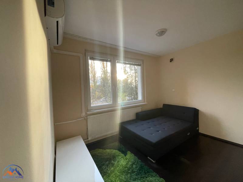 Einfaches Zimmer mit Bett, Teppich und Fenster in einer Einzimmerwohnung.