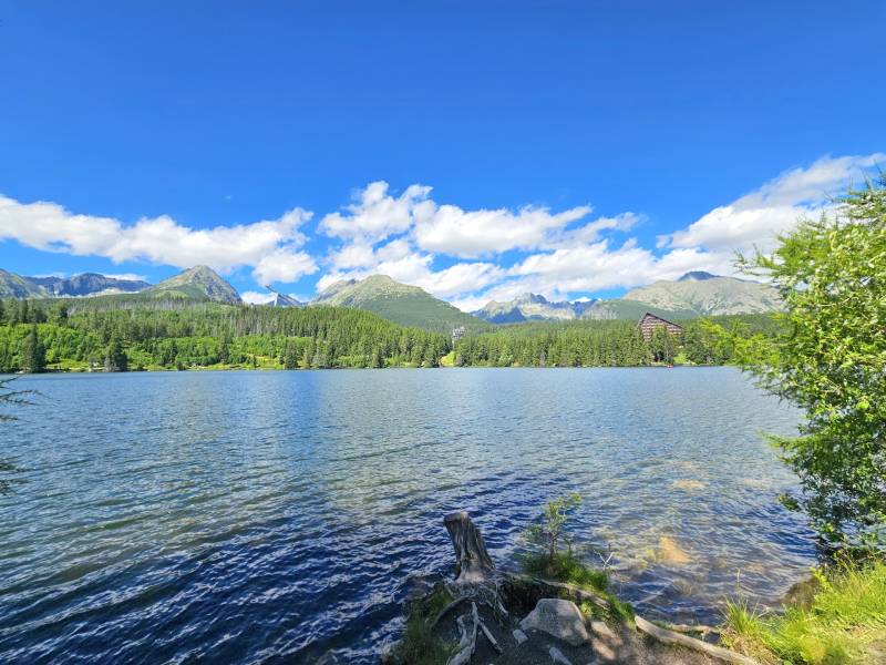 Der See in Štrba, umgeben von landwirtschaftlichen und forstwirtschaftlichen Flächen, mit Gebirgen und blauem Himmel.