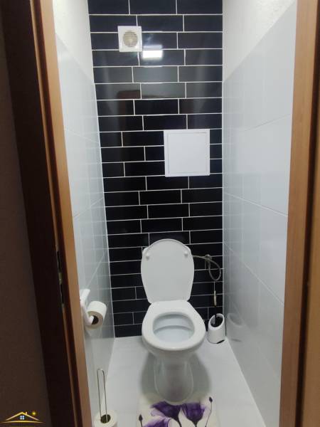 Eine Toilette mit schwarzen Fliesen in einer 3-Zimmer-Wohnung, ergänzt durch weiße sanitäre Ausstattung.