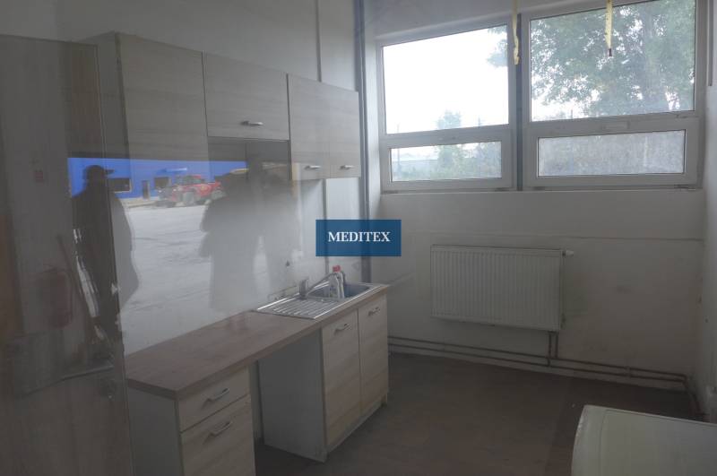 Küchenbereich mit Schränken, Spüle und Boden in Holzoptik in einem Lager- und Hallenumfeld.