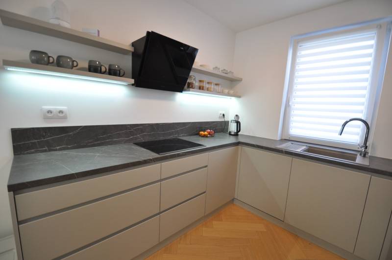 Eine Küche in einem Einfamilienhaus mit einer dunklen Arbeitsplatte und einem Boden in Holzoptik.