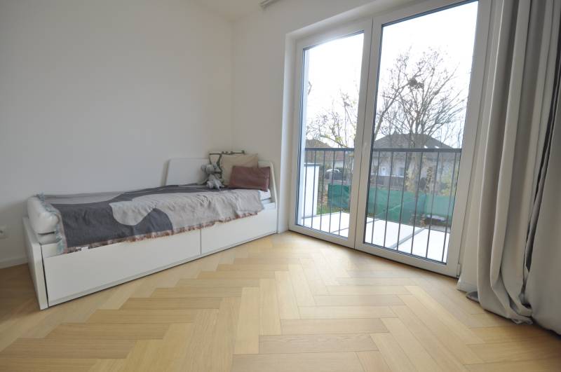 Ein Zimmer in einem Einfamilienhaus mit einem Bett, einem großen Fenster und einem Boden mit Holzdekor.