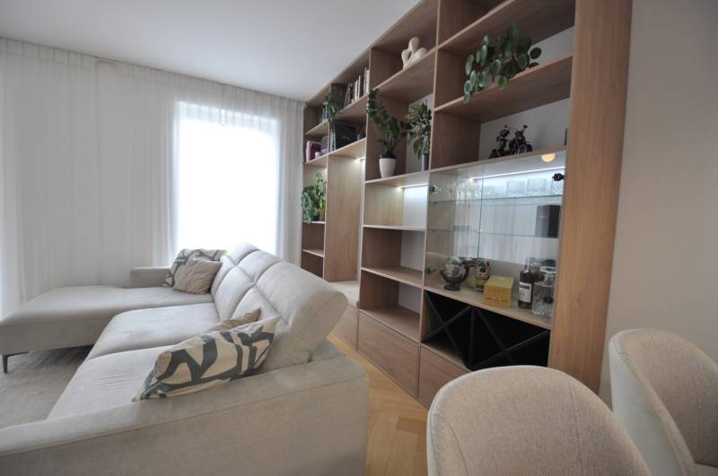 Wohnzimmer in einem Einfamilienhaus mit weißem Sofa, hölzernem Bücherregal und Pflanzen.