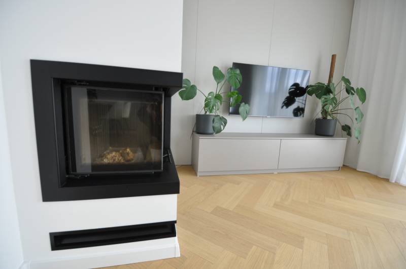 Wohnzimmer in einem Einfamilienhaus mit Kamin, Fernseher und Boden in Holzoptik.