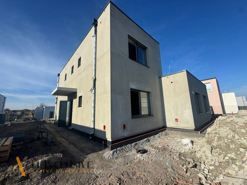 Ein im Bau befindliches Einfamilienhaus in Hubice mit minimalistischem Äußeren und benachbarten Gebäuden.