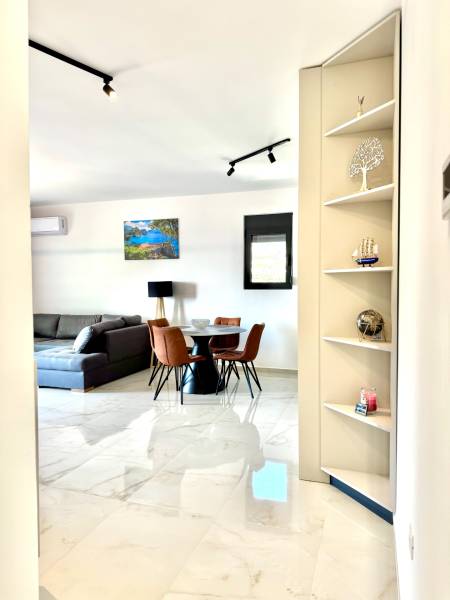 Innenraum einer Einzimmerwohnung mit weißem Boden, grauem Sofa und Esstisch.