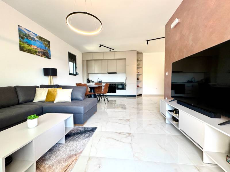 Wohnzimmer einer Einzimmerwohnung mit Sofa, Fernseher und Küchenzeile mit Sitzgelegenheit.