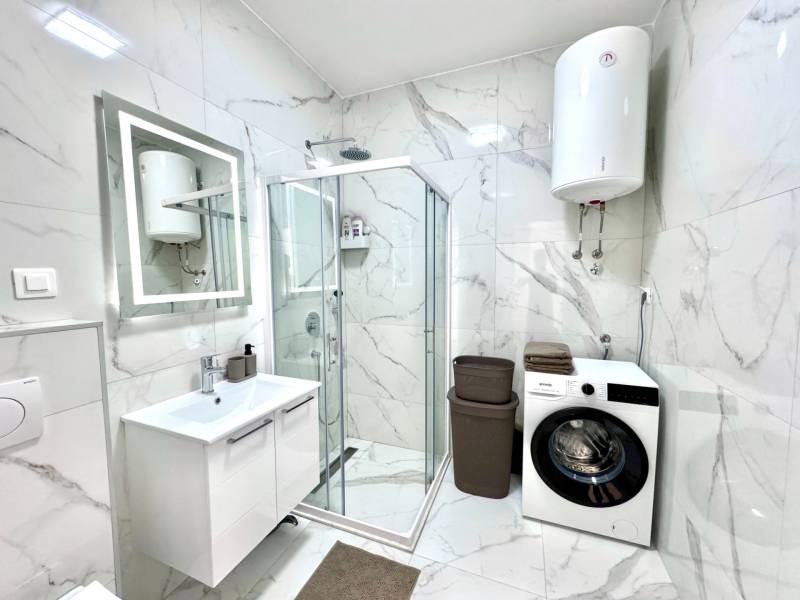 Badezimmer in einer Einzimmerwohnung mit Dusche, Waschmaschine und eleganten Marmorkacheln.