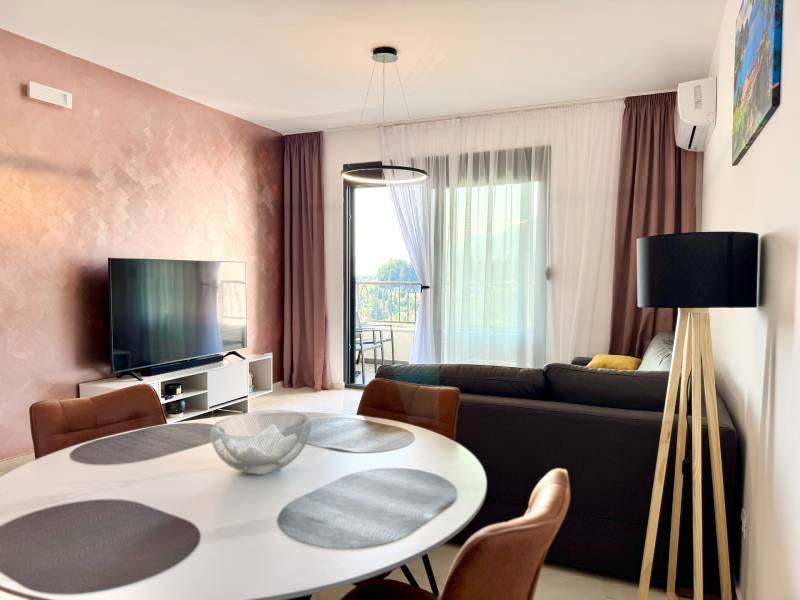 Wohnzimmer in einer Einzimmerwohnung mit Fernseher, Balkon und elegantem Tisch.