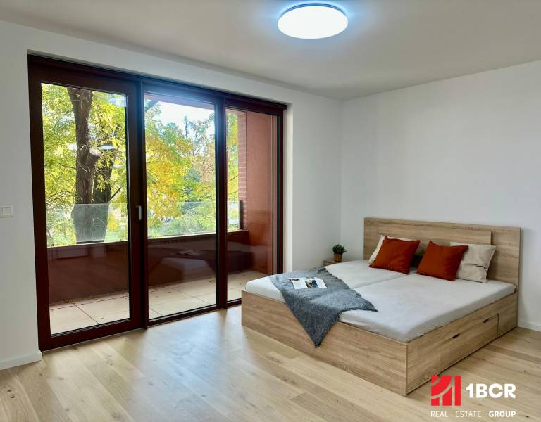 1-Zimmer-Wohnung mit großen Fenstern, Holzboden, Balkon und Bett.