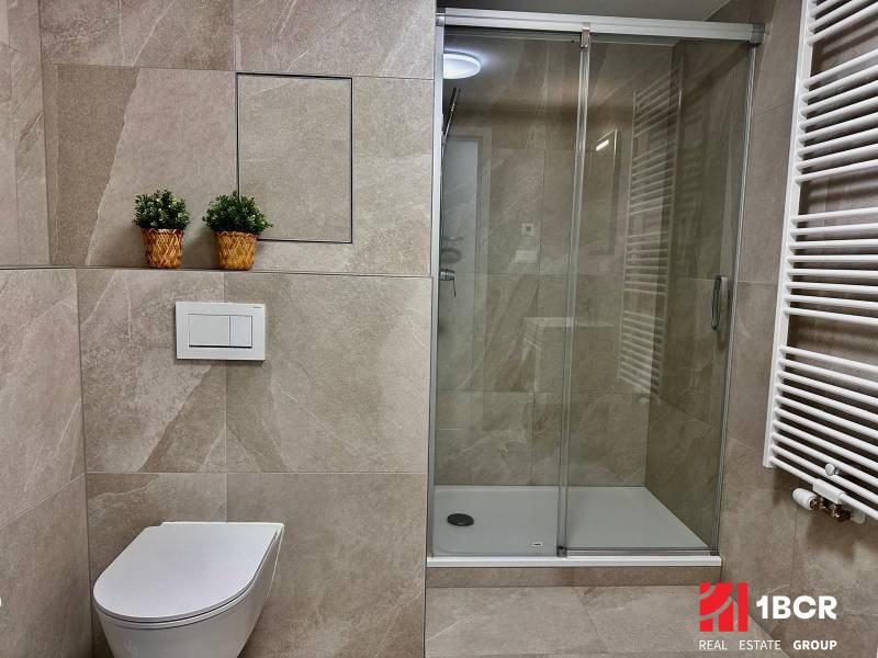 Badezimmer in einer Einzimmerwohnung mit Toilette, Duschkabine und lebenden Pflanzen in Körben.