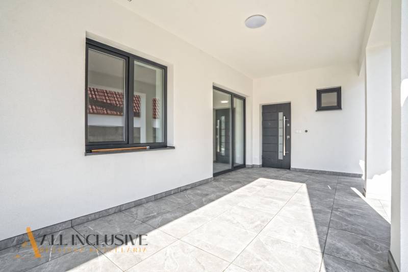 Ein Einfamilienhaus mit Terrasse, großen Fenstern und einem grauen Boden mit Fliesen.