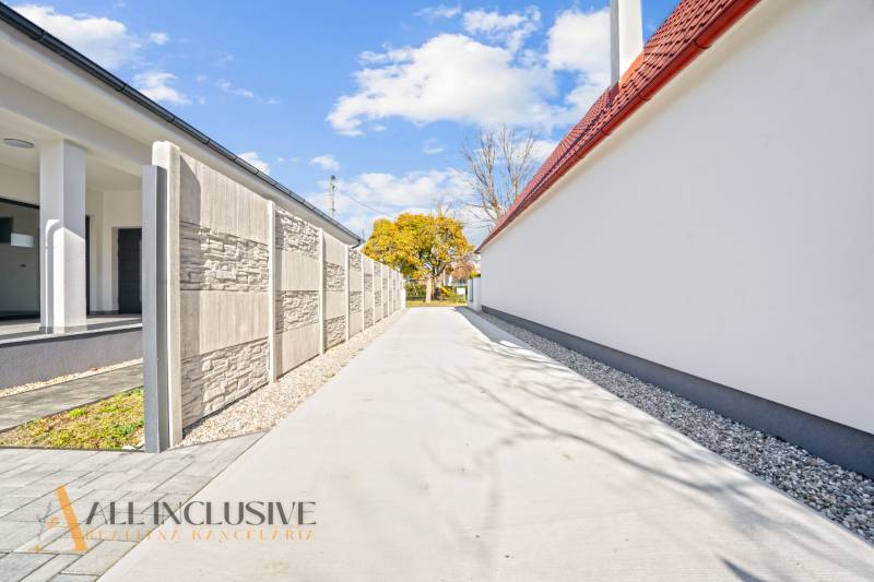 Eine schmale Zufahrtsstraße zwischen Einfamilienhäusern in Orechová Potôň, gesäumt von einer Mauer und Bäumen.