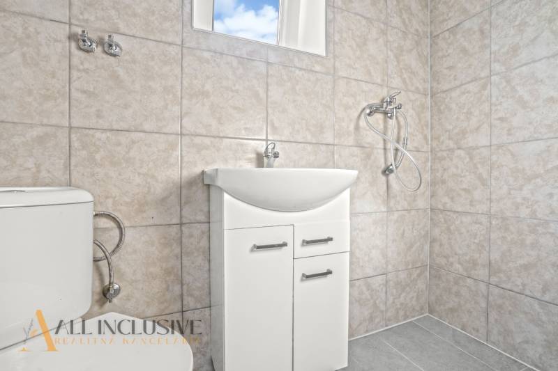 Ein Badezimmer in einem Einfamilienhaus mit Waschbecken, Dusche und Toilette in hellen Fliesen.