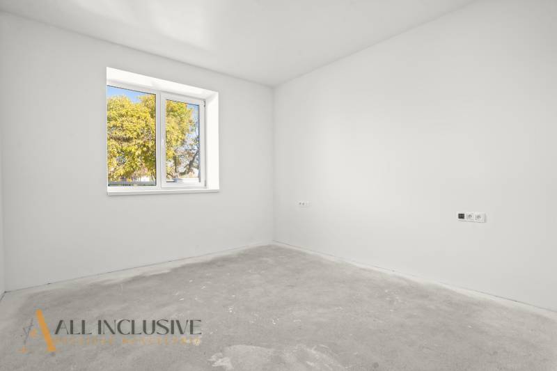 Ein leerer Raum in einem Einfamilienhaus mit weißen Wänden und einem Fenster mit Blick auf Bäume.